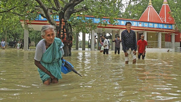 <div class="paragraphs"><p>An elderly women and other people walk through a flooded area after the Kankalitala Temple got partially submerged due to rains, in Birbhum district. </p></div>