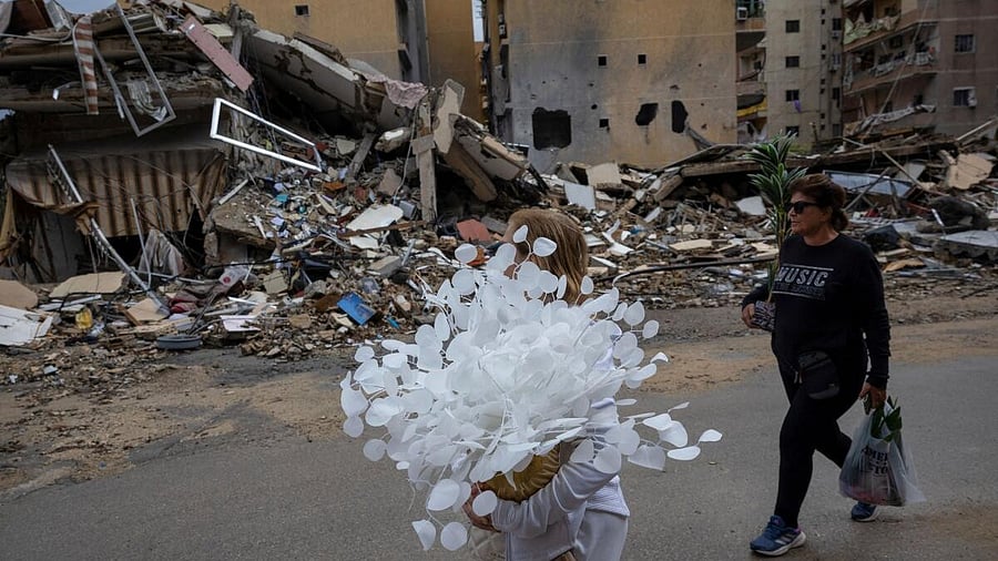 <div class="paragraphs"><p>A woman carries artificial flowers as she walks past a destroyed building, after a ceasefire between Israel and Iran-backed group Hezbollah took effect.</p></div>