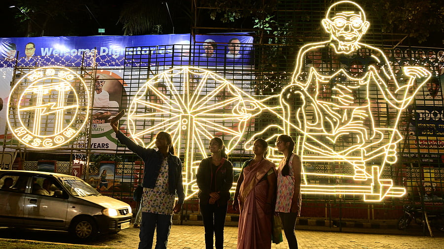 <div class="paragraphs"><p>Girls click a selfie before an illuminated image of Mahatma Gandhi on the occasion of ‘Gandhi Bharath’ event, in Belagavi on Thursday. </p></div>
