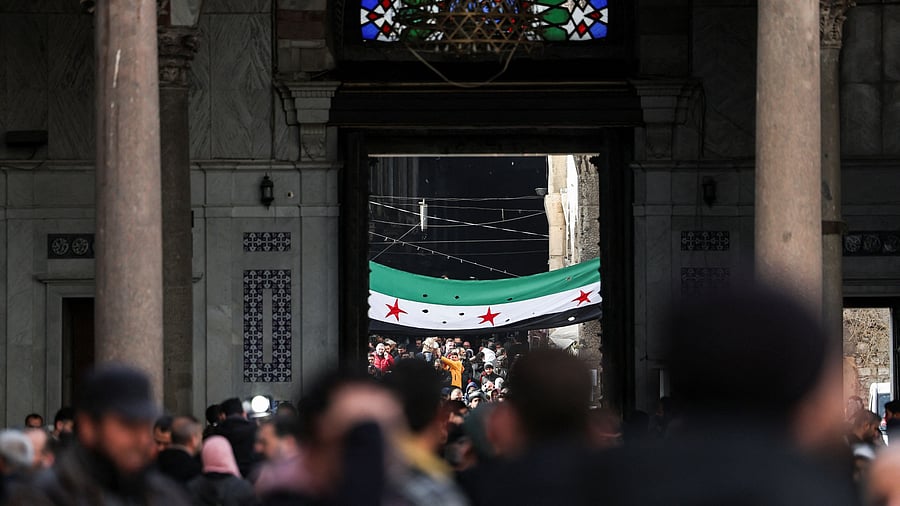<div class="paragraphs"><p>People walk as a flag adopted by the new Syrian rulers is seen, in the Umayyad Mosque, after Syria's Bashar al-Assad was ousted, in Damascus, Syria, December 27, 2024. </p></div>