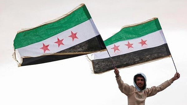 <div class="paragraphs"><p>A person holds flags adopted by the new Syrian rulers, in Damascus</p></div>
