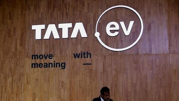 <div class="paragraphs"><p>A man stands next to a sign of the brand of Tata Motors' passenger electric vehicles 'Tata.ev '</p></div>