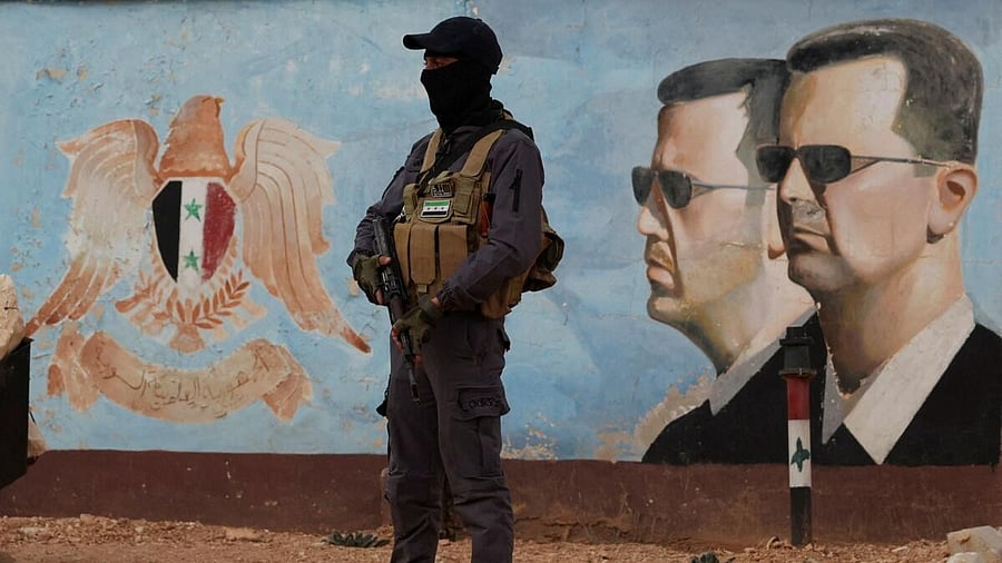 <div class="paragraphs"><p>A member of the former rebel group Hayat Tahrir al-Sham stands guard near an image of Syria's Bashar al-Assad at the fourth division headquarters in Damascus.</p></div>