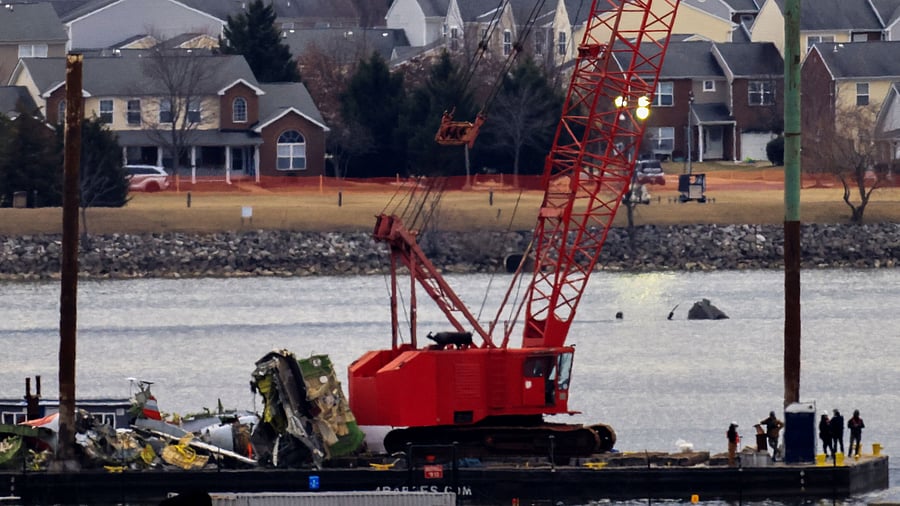<div class="paragraphs"><p>A barge carrying a crane transports parts of the wreckage from the Potomac River as they cross past the helicopter involved in the crash, in the aftermath of the collision of American Eagle flight 5342 and a Black Hawk helicopter that crashed into the river, by the Ronald Reagan Washington National Airport</p></div>