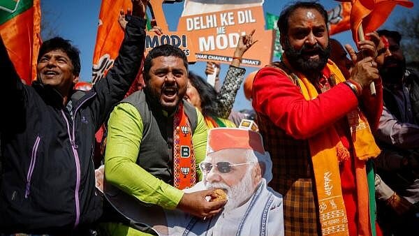 <div class="paragraphs"><p>A BJP supported holds a laddu on the face of PM Modi's poster.</p></div>