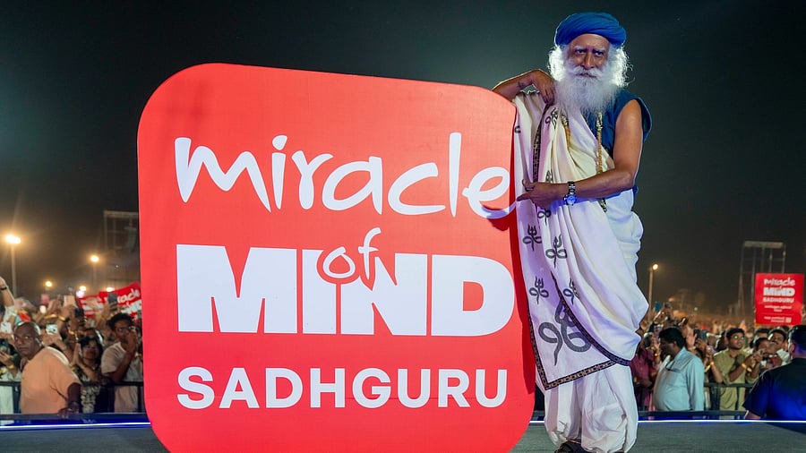 <div class="paragraphs"><p>Sadhguru seen next to a sign with his app's name on it</p></div>