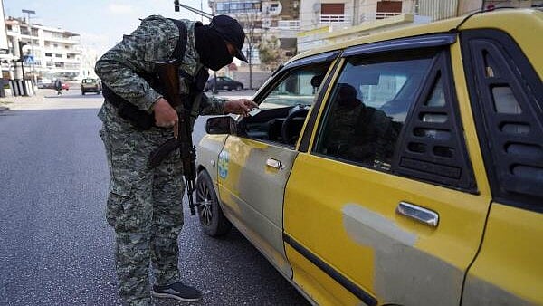 <div class="paragraphs"><p>A member of the Syrian security forces checks an ID of a person, in Latakia</p></div>