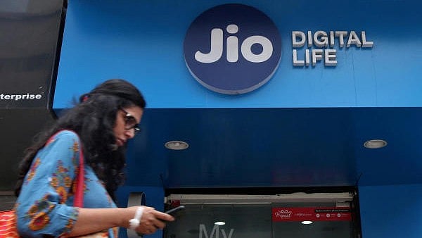 <div class="paragraphs"><p>A woman checks her mobile phone as she walks past a mobile store of Reliance Industries' Jio telecoms unit in Mumbai</p></div>