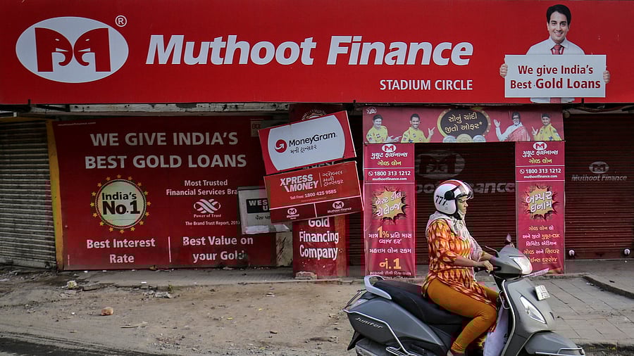 <div class="paragraphs"><p> A woman rides her scooter past a Muthoot Finance branch</p></div>