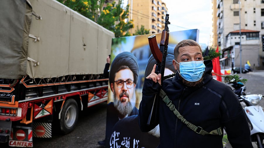<div class="paragraphs"><p>File Photo: A man holds a weapon next to a poster with an image of late senior Hezbollah official Hashem Safieddine, at the entrance of Beirut's southern suburbs.</p></div>