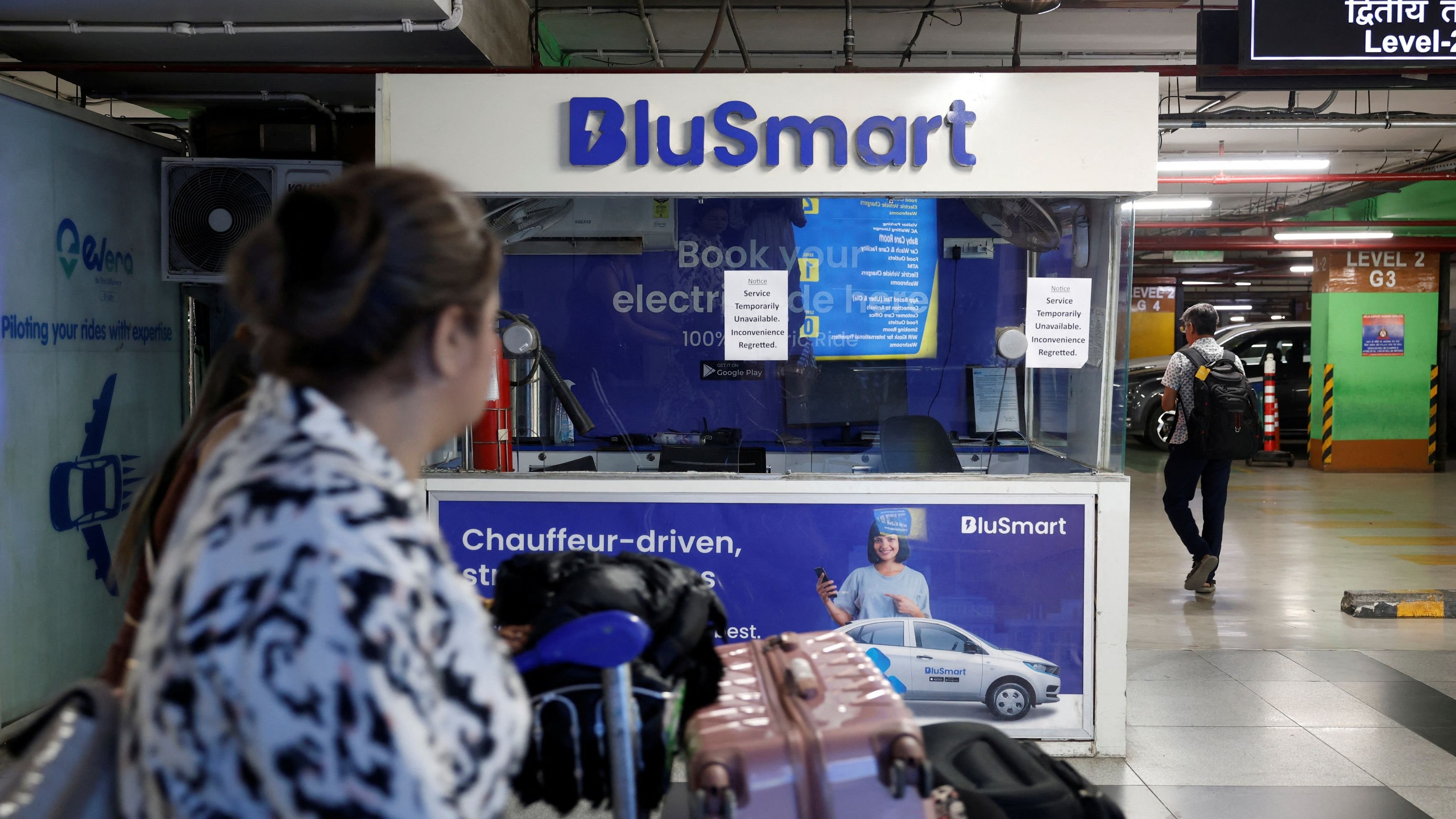 <div class="paragraphs"><p>Travellers move past a closed BluSmart electric car booking counter at T3 parking lot at the Indira Gandhi International Airport in New Delhi</p></div>