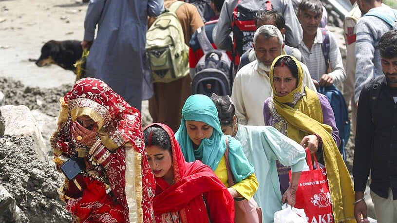 <div class="paragraphs"><p>A newly-wed woman along with others walks towards her destination after the Jammu-Srinagar National Highway was blocked by debris following heavy rain trigged landslides and flash flood, in Ramban</p></div>