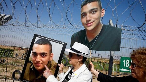 <div class="paragraphs"><p> Varda Ben Baruch, grandmother of hostage Edan Alexander, points at the portrait of Edan, as family members and supporters of hostages who were kidnapped during the deadly October 7 attack, stand near the kibbutz defence on the day they use giant loudspeakers to call their captive loved ones over the border between Israel and Gaza, at Kibbutz Nir Oz, in southern Israel.</p></div>