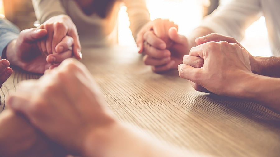 Cropped image of beautiful business team holding hands and praying while sitting in office