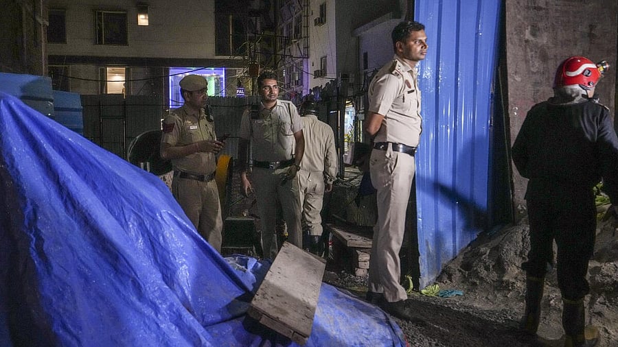 <div class="paragraphs"><p>Police personnel and others stand near the site where a wall of a basement at an under-construction building collapsed at Paharganj area, in New Delhi, Saturday. </p></div>