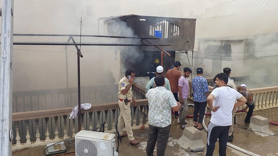 <div class="paragraphs"><p>A police official and others stand as smoke billows from a building after a fire broke out, in Hyderabad, Telangana, Sunday, May 18, 2025.</p></div>