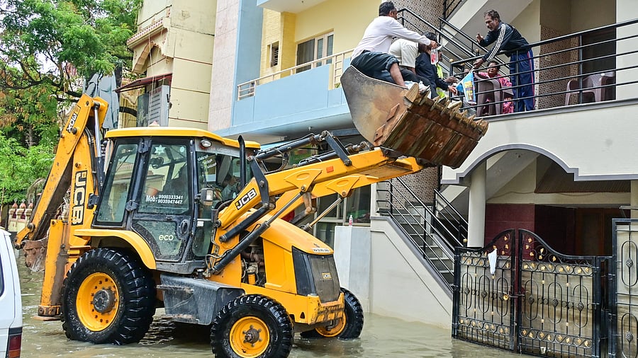 <div class="paragraphs"><p>BBMP staff use an excavator to distribute essentials to residents of Sai Layout on Tuesday. </p></div>