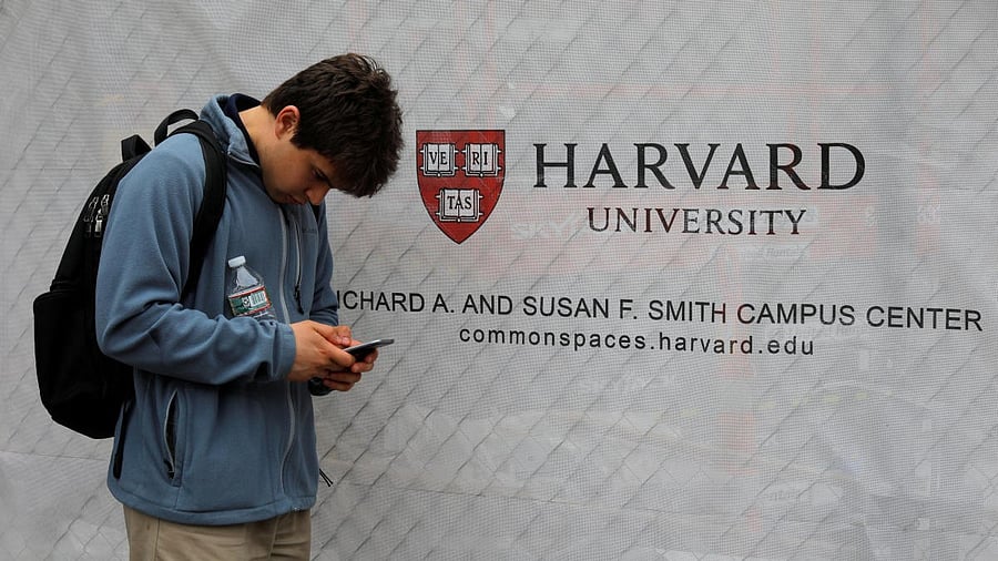 <div class="paragraphs"><p>A man looks at his mobile phone beside a sign for Harvard University.</p></div>