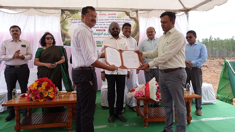 <div class="paragraphs"><p>KFDC officer Suresh (L) hands over documents to N Ravindrakumar, Bengaluru Urban Deputy Conservator of Forests, to mark the return of 154 acres of reserved forest land, leased to the corporation, at an event in Madappanahalli plantation on Monday. Forest Minister Eshwar Khandre (C) and senior officials discussed the best approach to turn the land into a lung space.</p></div>