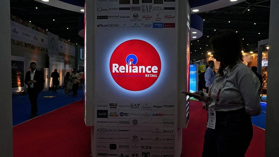 <div class="paragraphs"><p> A woman checks her phone next to a Reliance Retail kiosk.</p></div>