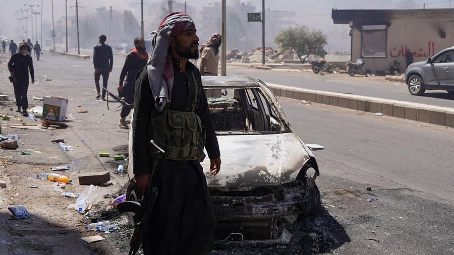 <div class="paragraphs"><p>A Bedouin fighter stands near a damaged car, following the Syrian presidency's announcement of a ceasefire after days of violence in Sweida province triggered by clashes between Bedouin fighters and Druze factions, in Sweida, Syria.</p></div>