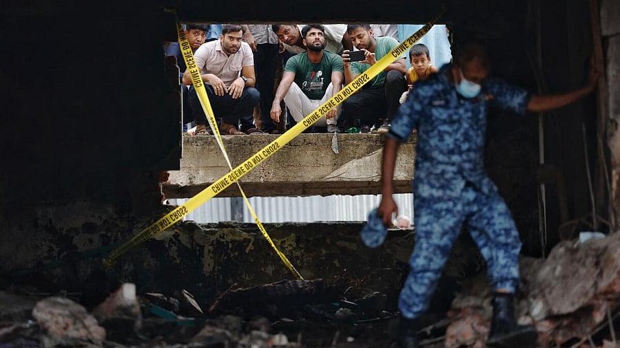 <div class="paragraphs"><p>People watch through a damaged window as a member of Bangladesh Air Force works at a site, after an air force training aircraft crashed into a building belonging to Milestone School and College, in Dhaka, Bangladesh, July 22, 2025.</p></div>