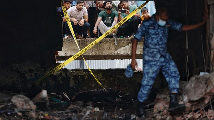 <div class="paragraphs"><p>People watch through a damaged window as a member of Bangladesh Air Force works at a site, after an air force training aircraft crashed into a building belonging to Milestone School and College, in Dhaka, Bangladesh.</p></div>