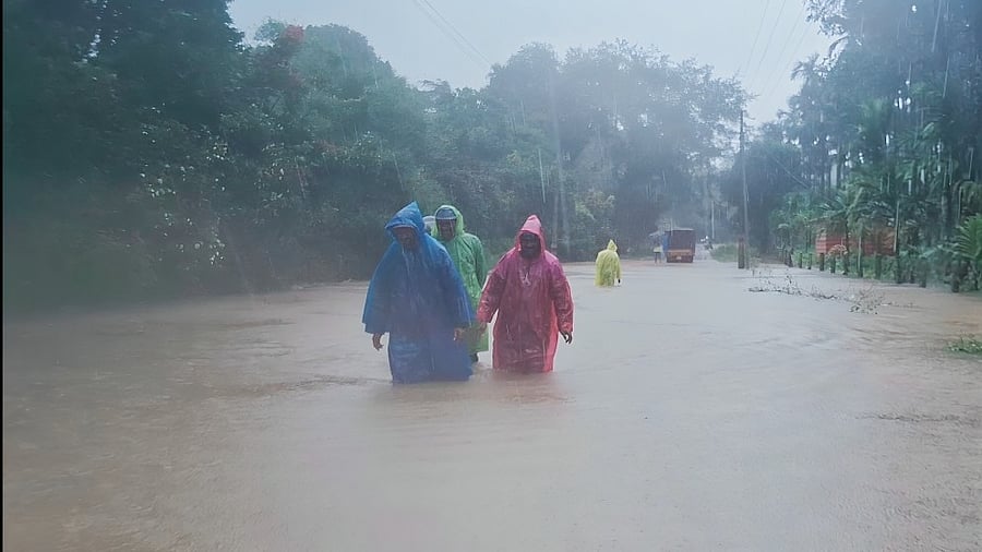 People wade through a waist-high water to cross the overflowing Malathi river at Naabal village in Thirthahalli taluk, Shivamogga district on Saturday.