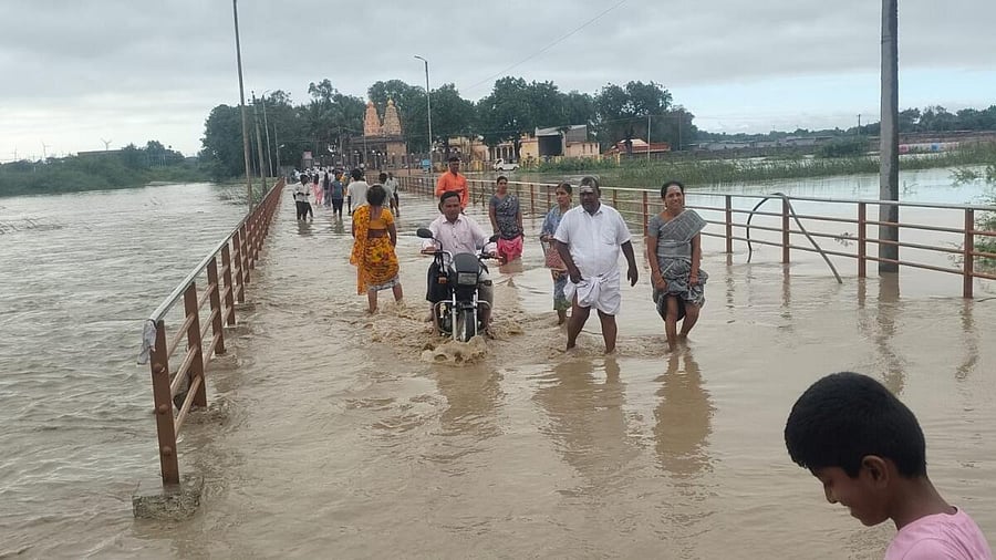 People wade through the flooded bridge across Hirehalla stream to reach Vijaya Mahantesh Gadduge on the outskirts of Ilkal town, Bagalkot district. The town received heavy rain on the intervening night of Tuesday and Wednesday.