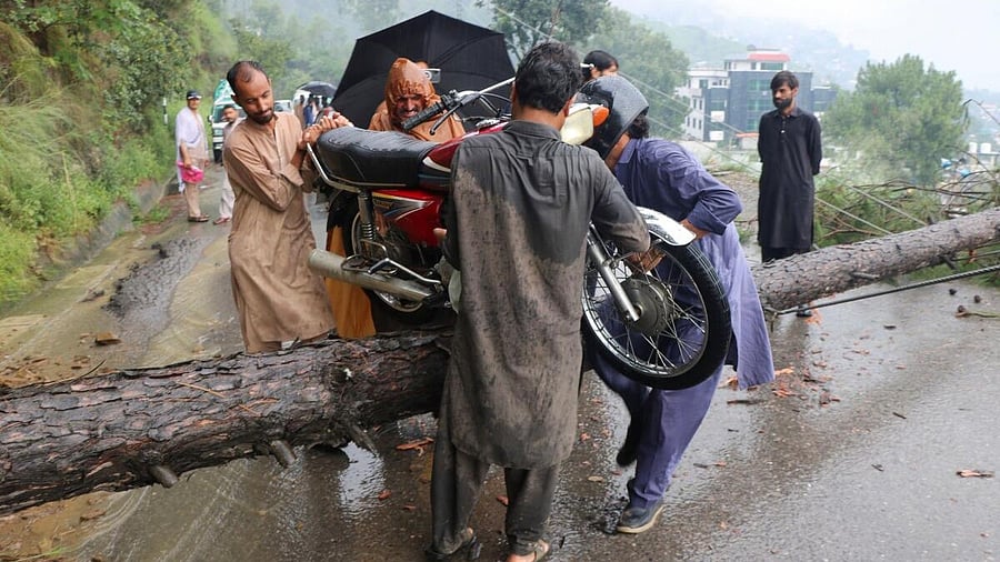 <div class="paragraphs"><p>Residents move a motorcycle over a fallen tree which blocked the road amid heavy rains</p></div>
