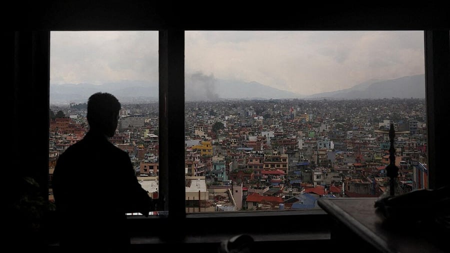 <div class="paragraphs"><p>A person looks out of a window as smoke rises during a protest against Monday's killing of 19 people after anti-corruption protests that were triggered by a social media ban, which was later lifted, during a curfew in Kathmandu, Nepal.</p></div>