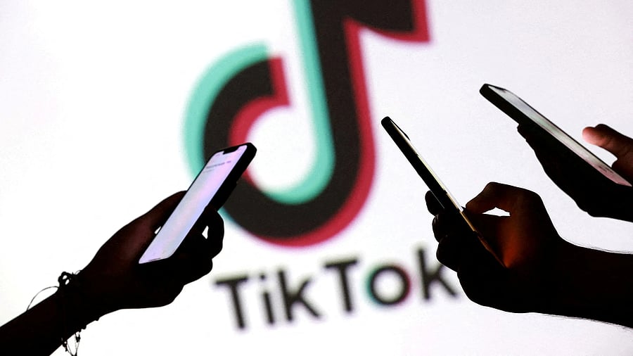 FILE PHOTO: FILE PHOTO: Teenagers pose for a photo while holding smartphones in front of a TikTok logo in this illustration taken September 11, 2025. REUTERS/Dado Ruvic/Illustration/File Photo/File Photo