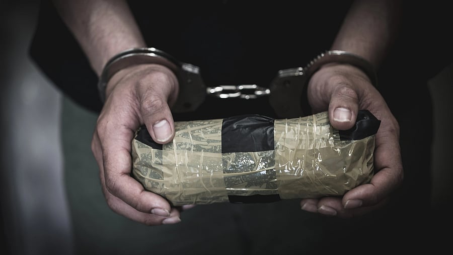 <div class="paragraphs"><p>Image showing the person in handcuffs a holding a taped bag.</p></div>