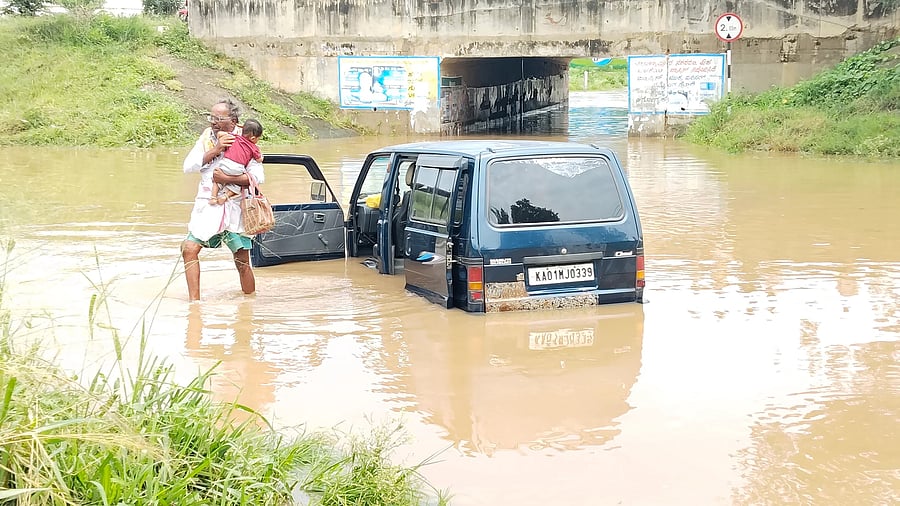 <div class="paragraphs"><p>An elderly man carries a baby to safety after an Omni gets trapped in the floods near an underpass on Chikkaballapur-Manchanabele road on Friday. Many parts of Chikkaballapur district received sharp showers in the intervening night of Thursday and Friday. </p></div>