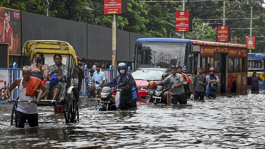 <div class="paragraphs"><p>Commuters make their way through a flooded road after heavy rainfall, in Kolkata</p></div>
