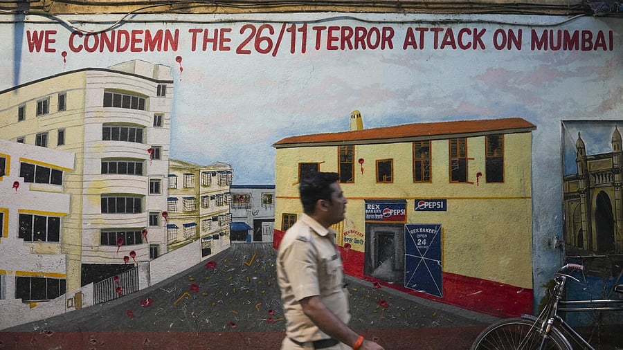 <div class="paragraphs"><p>A police constable walks past a mural depicting Nariman House</p></div>