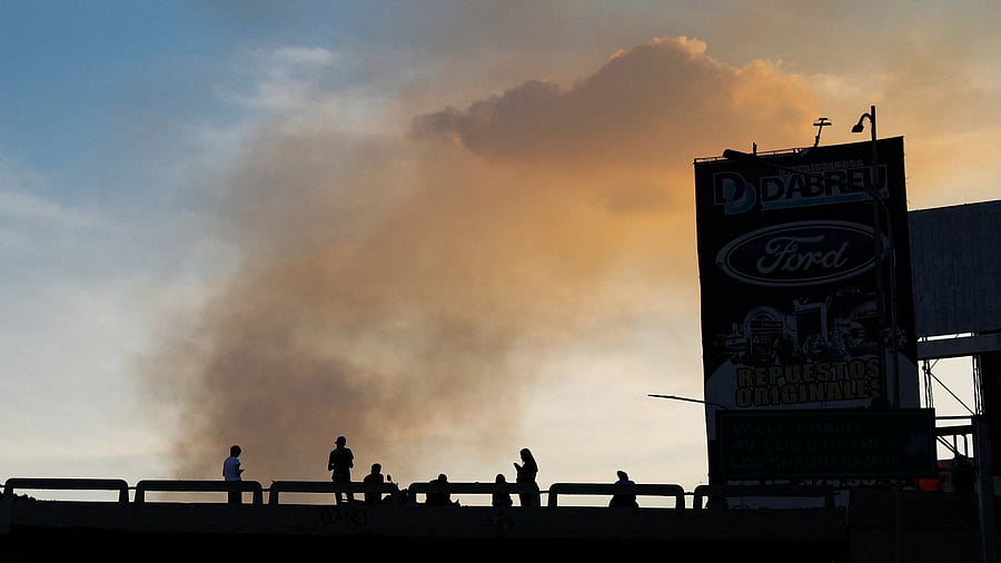 <div class="paragraphs"><p>People on a bridge are silhouetted as smoke rises near Fort Tiuna.</p></div>
