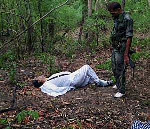 An Indian security person stands near the body of one of the victims of Saturday's Maoist attack in a densely forested area in Bastar, about 345 kilometers (215 miles) south of Raipur, Chhattisgarh state, India, Sunday, May 26, 2013. Officials reacted with outrage Sunday to an audacious attack by about 200 suspected Maoist rebels who set off a roadside bomb and opened fire on a convoy carrying Indian ruling Congress party leaders and members in an eastern state, killing at least 24 people and wounding 37 others. (AP Photo)