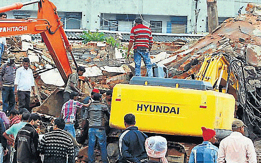 A huge cement tank collapsed on the excavator killing the operator on the spot near old bus stand in Hassan, on Tuesday. DH PHOTO