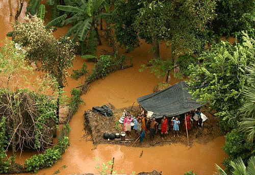 People wait for relief material on the top of a thatch in a flooded locality after heavy rains in the aftermath of Cyclone Phailin in Balasore on Monday. PTI Photo