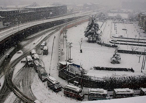 Buses ply on roads during heavy snowfalls at Jahangeer Chowk in Srinagar on Wednesday. PTI Photo