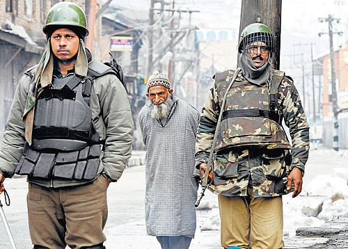 Clamped down: An elderly Kashmiri civilian walks as paramilitary soldiers stand guard in Srinagar on Sunday. AP