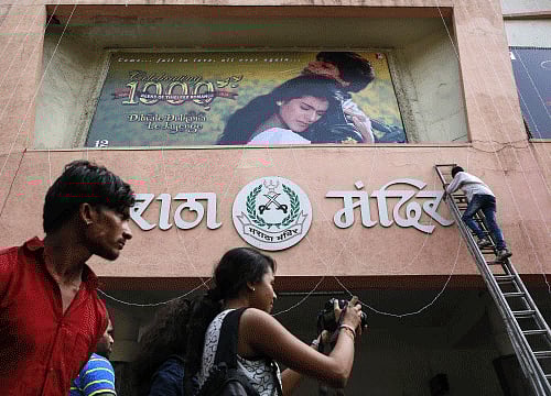 Cinema goer takes pictures as an employee prepares a hoarding of Bollywood movie 'Dilwale Dulhania Le Jayenge' outside Maratha Mandir theatre in Mumbai. Reuters