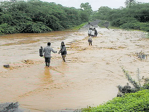 Local residents wade through water overflowing on a bridge at Aralichandi village near Basavana Bagewadi in Vijayapura district on Wednesday. DH PHOTO
