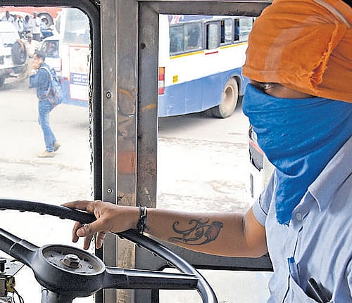 Fear of reprisal: Policemen guard a bus at the Kempegowda bus stand. (Right) A driver covers his face to conceal his identity as the BMTC resumed skeletal service from Shanthinagar to Majestic. DH Photo