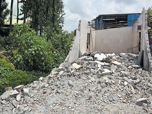 Owners of an industrial unit on Lakshmipura main road in Abbigere on Monday demolish a portion of their premises that had come up on a stormwater drain. dh photo