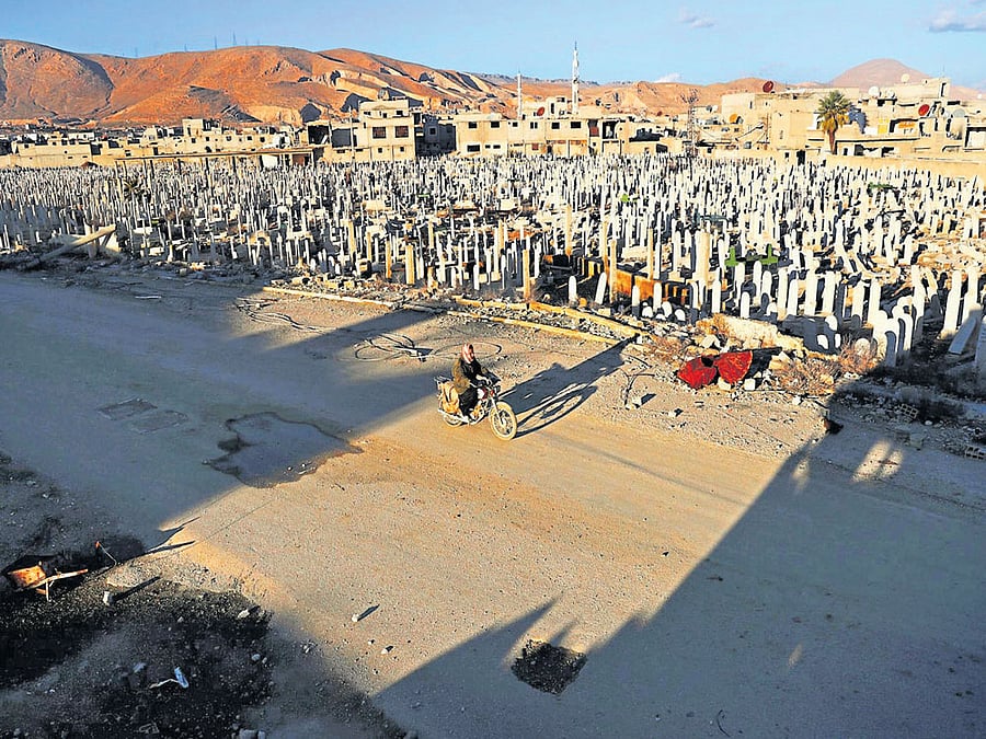 town of the dead: A Syrian man rides a motorbike past a cemetery in the rebel-held town of Douma in Damascus. Upward of 5,00,000 are dead from the war and close to half the population of Syria is either internally or externally displaced. afp