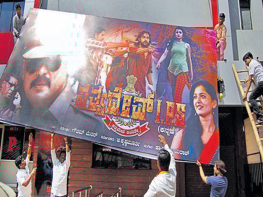 Anti-dubbing activists remove the banner of Satyadev IPS at Roopam theatre in Hubballi on Friday. DH photo