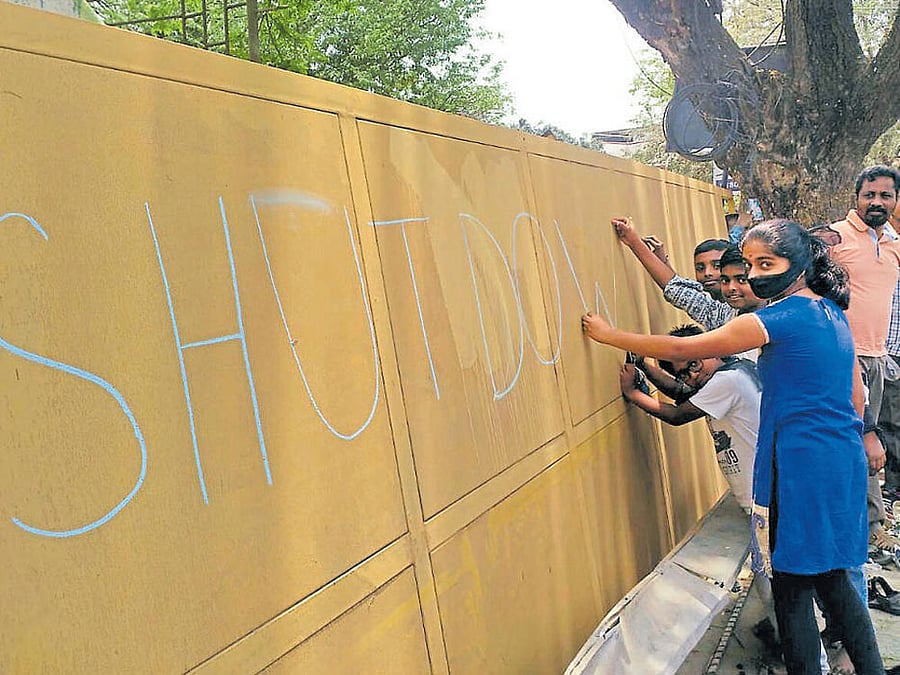 Protesters scribble a message on the compound wall of the KCDC plant in Somasundarapalya on Sunday, demanding its closure. DH Photo