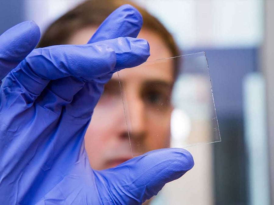Graduate student Nicholas Davy holds a sample of the special window glass, which harvests one portion of the light spectrum to control other parts of the spectrum. Specifically, it uses near-ultraviolet light to generate electricity, which powers chemical reactions that lighten or darken the glass as needed. When darkened, the window can block more than 80 percent of light.    Photo by David Kelly Crow. Photo via Princeton University. Link: https://goo.gl/CR2BXr
